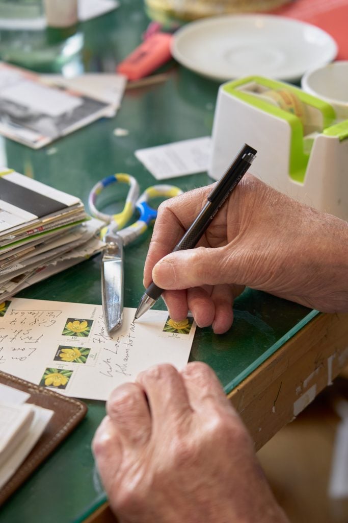 This image depicts the hands belong to an old person writing postcards