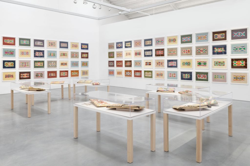 many artworks with native american designs installed on a gallery wall, with vitrines in the middle of the room holding additional works