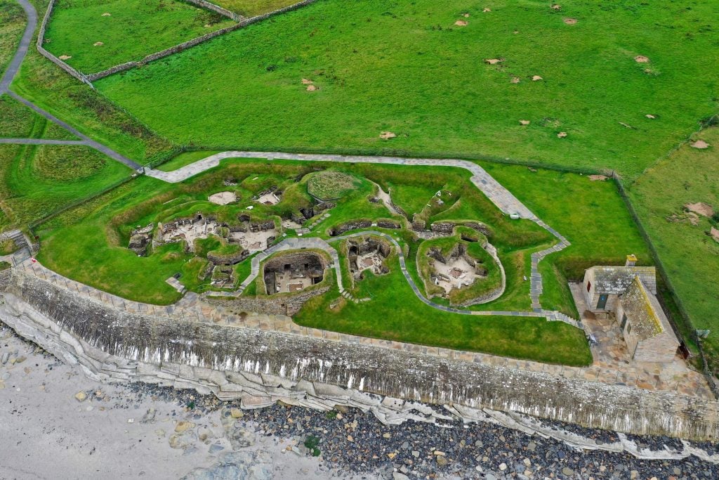 an aerial photograph of Skara Brae showing the rounds of houses among green fields