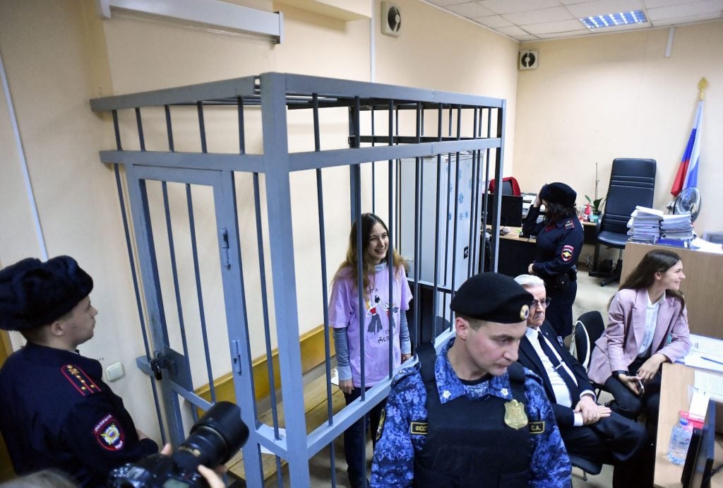 A woman in a pink shirt inside a cage in a court room