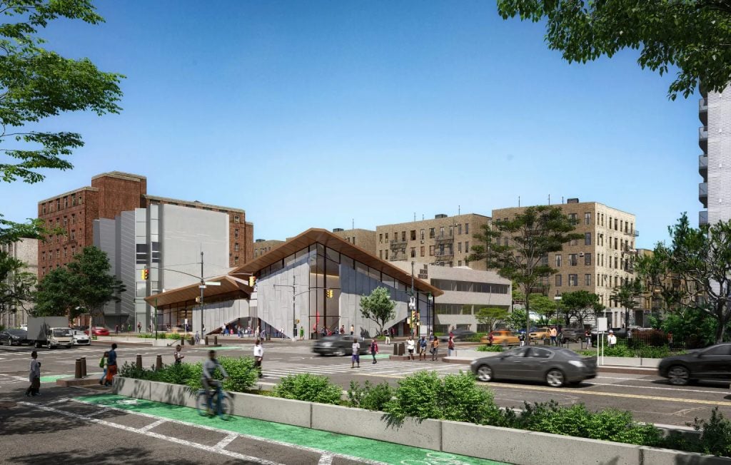 The firm Marvel's architectural rendering of the expanded Bronx Museum with its new entrance and three-story lobby on Grand Concourse and 165th Street. In shows the museum behind the bike lane and planted median in the center of the street, with blue skies behind it. The contemporary looking building has a brown peaked roof on the corner, with a glass and concrete facade.