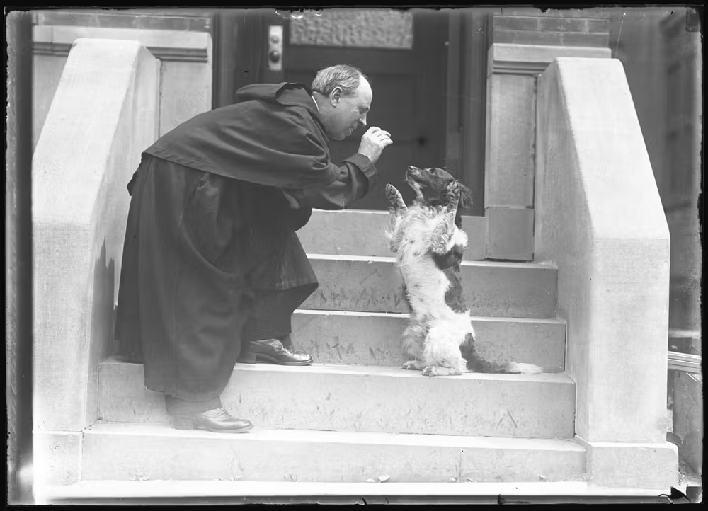a priest gives a treat to a dog on the steps outside a house