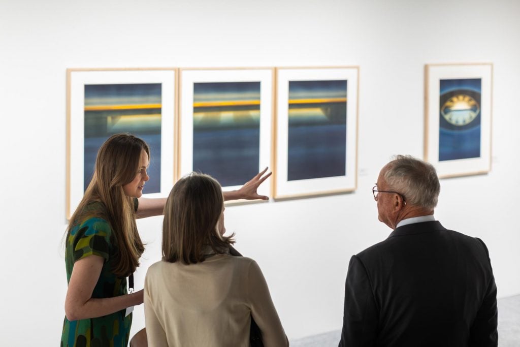 An art dealer speaking to a couple gestures to artworks on the wall