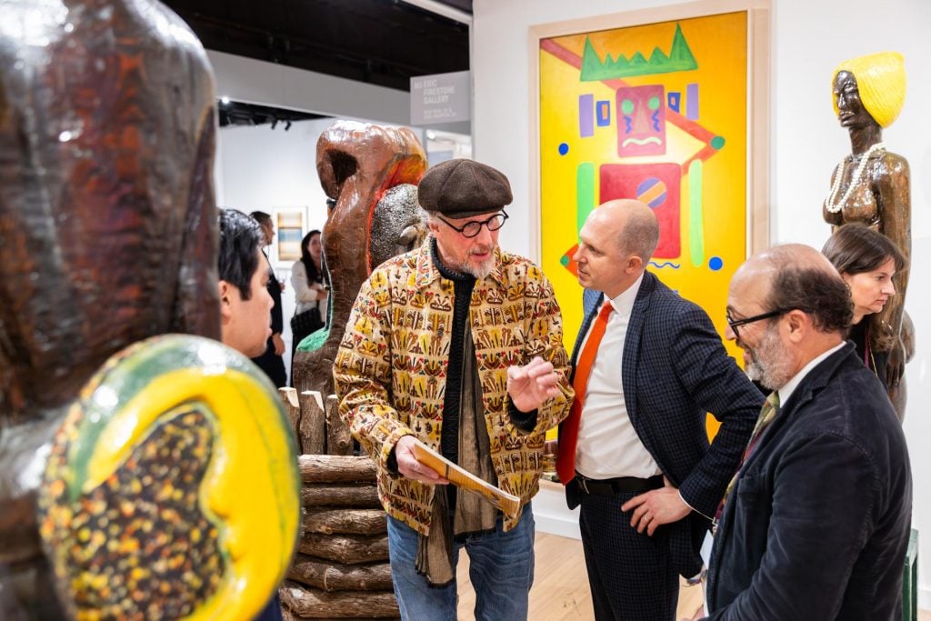 Three men engage in a conversation, with several artworks in view