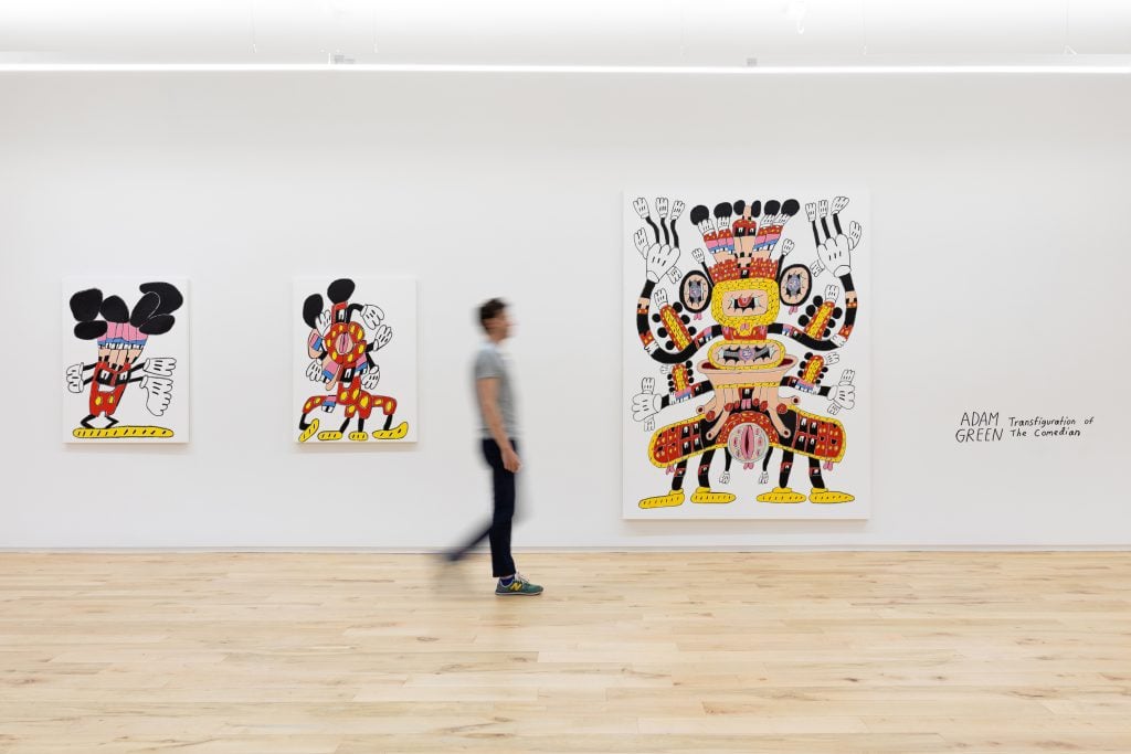 A man walking through a gallery hung with three colored pencil canvases with bright colors