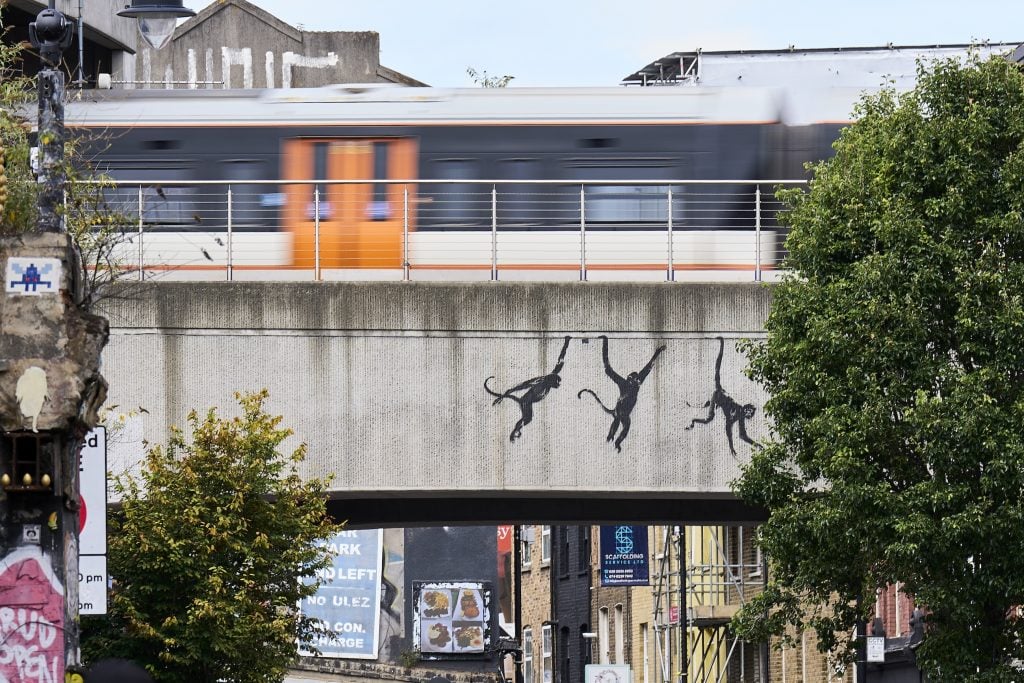 Three painted monkeys swing along the side of a railway overpass in South London