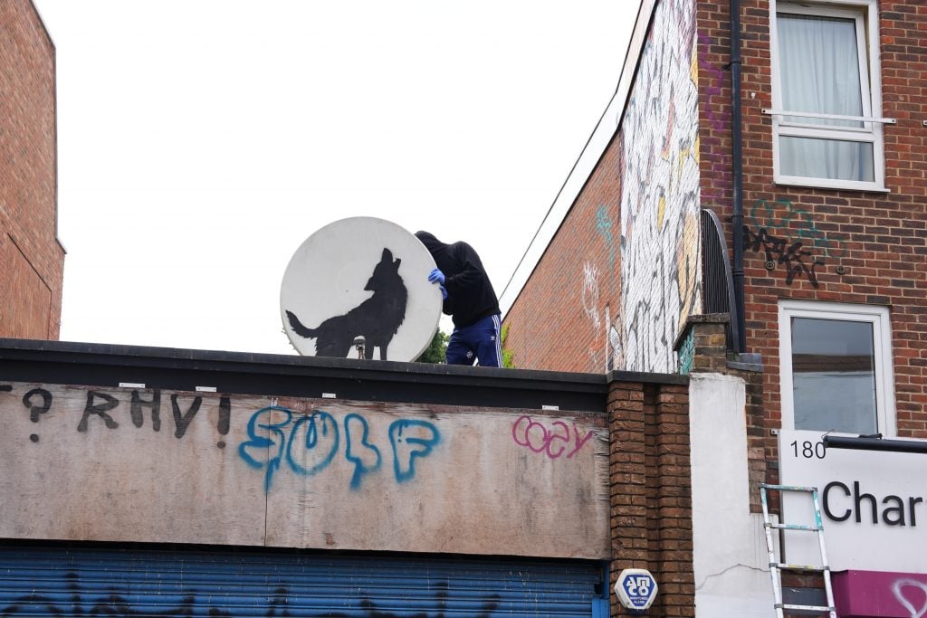 a man tries to remove a satellite dish with an image of a wolf on it from a building's roof