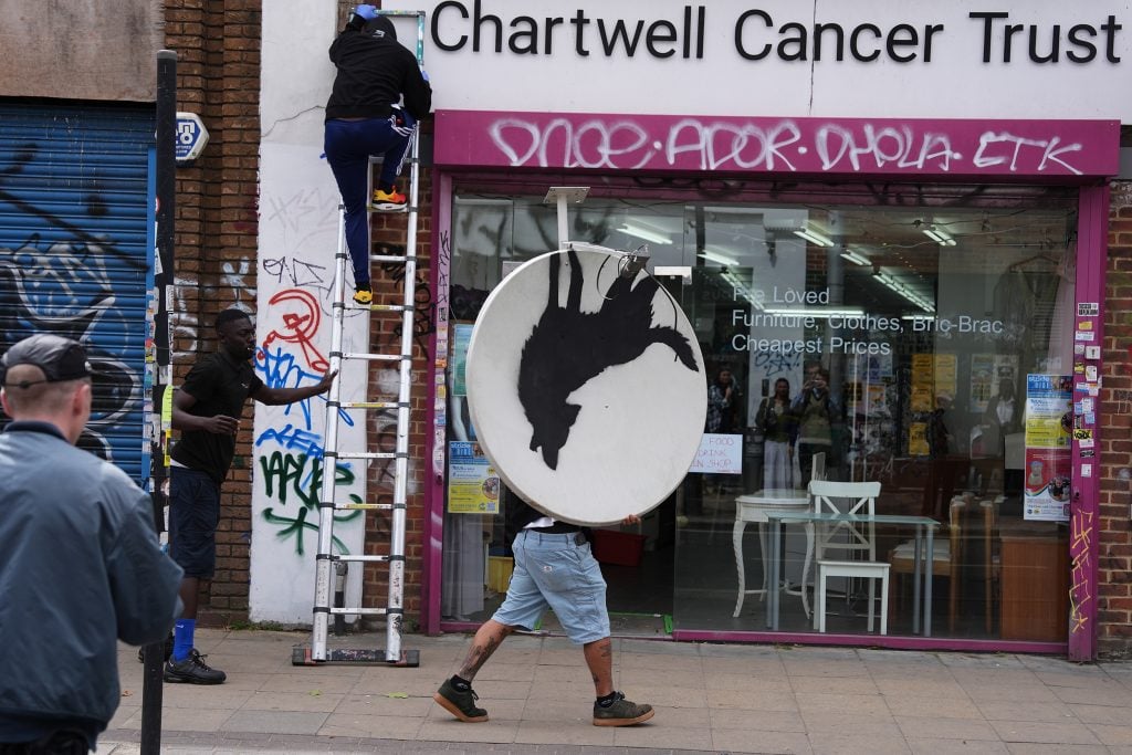 a man walks along a street with a satellite dish on which is an image of a wolf, upside down