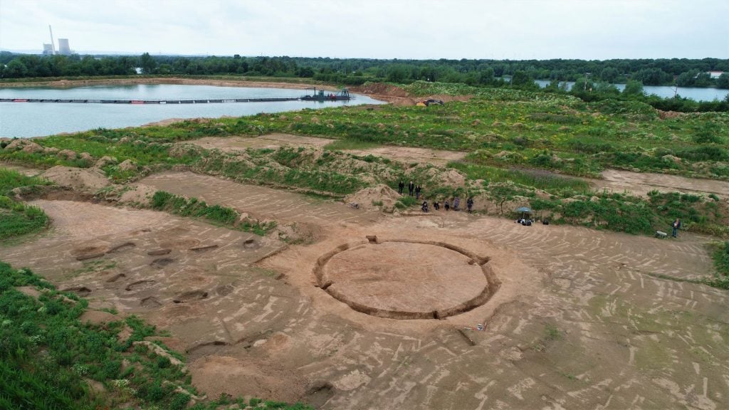a drone photo of the site with a circular ditch visible surrounded by adjacent burial pits