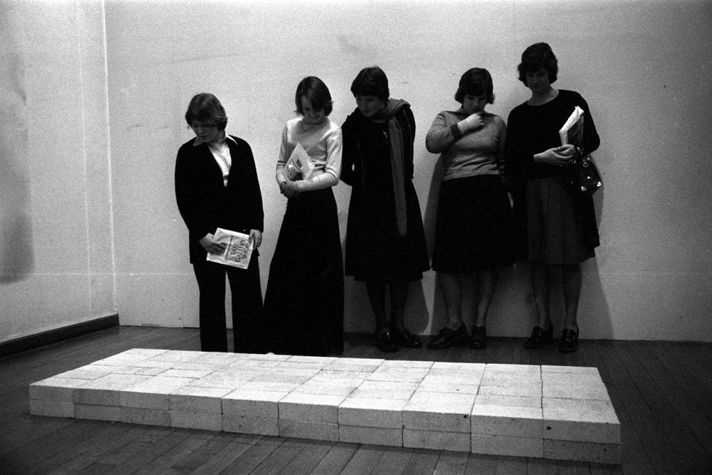 Five schoolgirls looking at a sculpture by Carl Andre comprising a rectangular formation of bricks