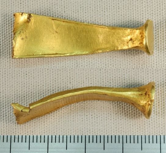 A photograph of two gold bracelet fragments laid alongside a ruler for scale
