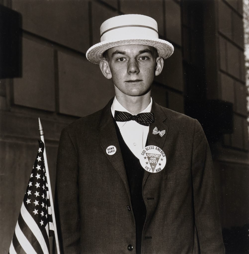 A photo of a boy in a straw hat and a suit holding a U.S. flag