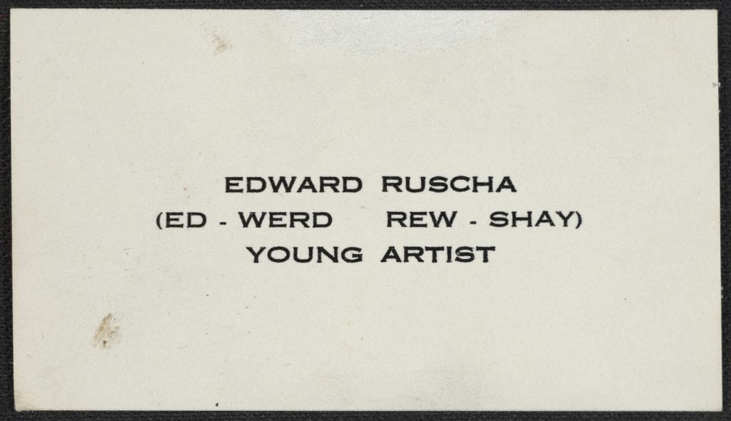 An image of a simple, white business card imprinted with the name Edward Ruscha, a phoenetic pronounciation, and 