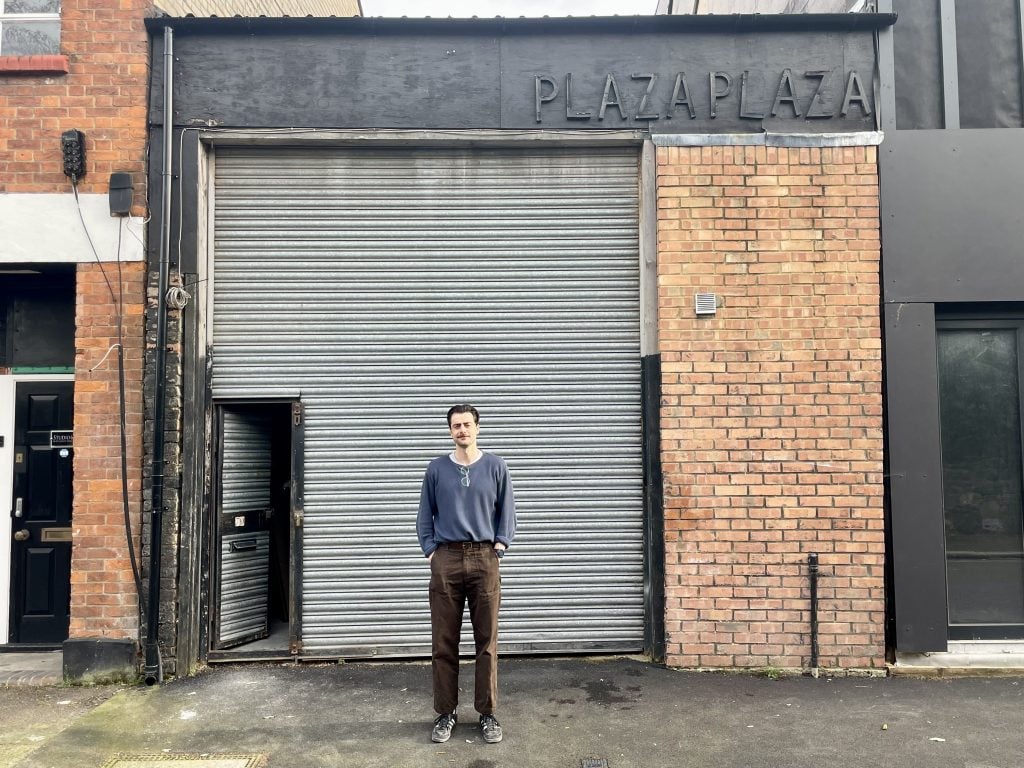 a man stands in front of a brick building with a steel roll-down gate pulled down