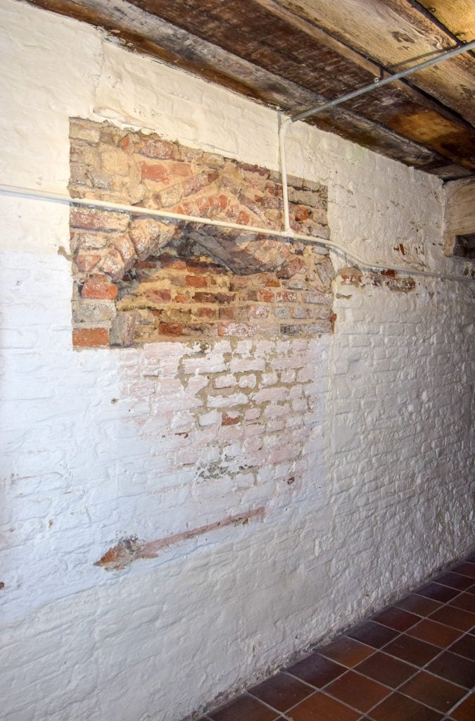 A white brick wall with a small rectangle of red brick showing the imprint of an ancient archway that may have led to Shakespeare's dressing room.