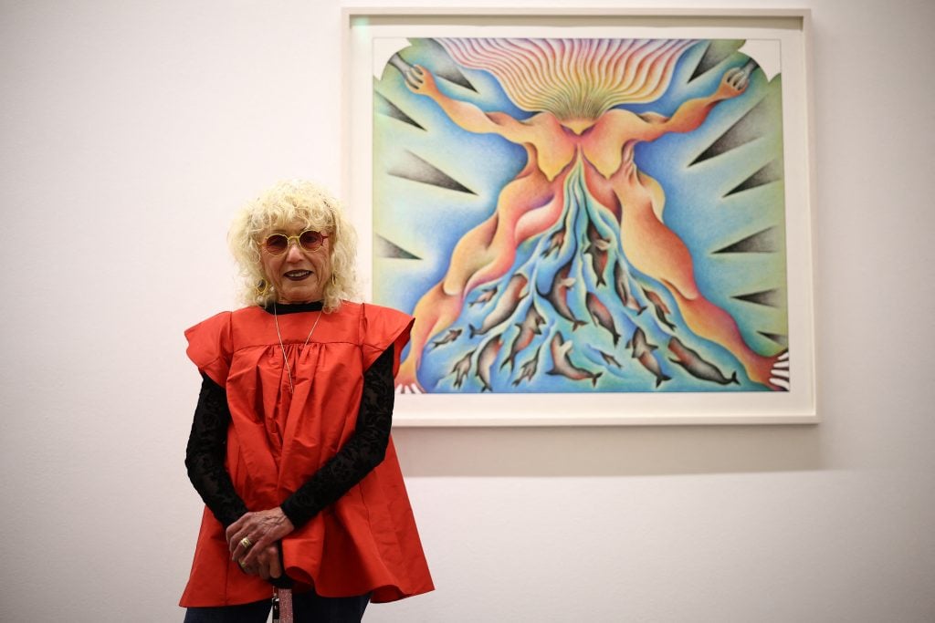 a woman in a loose red dress stands in front of a semi-abstract artwork hanging on a white wall