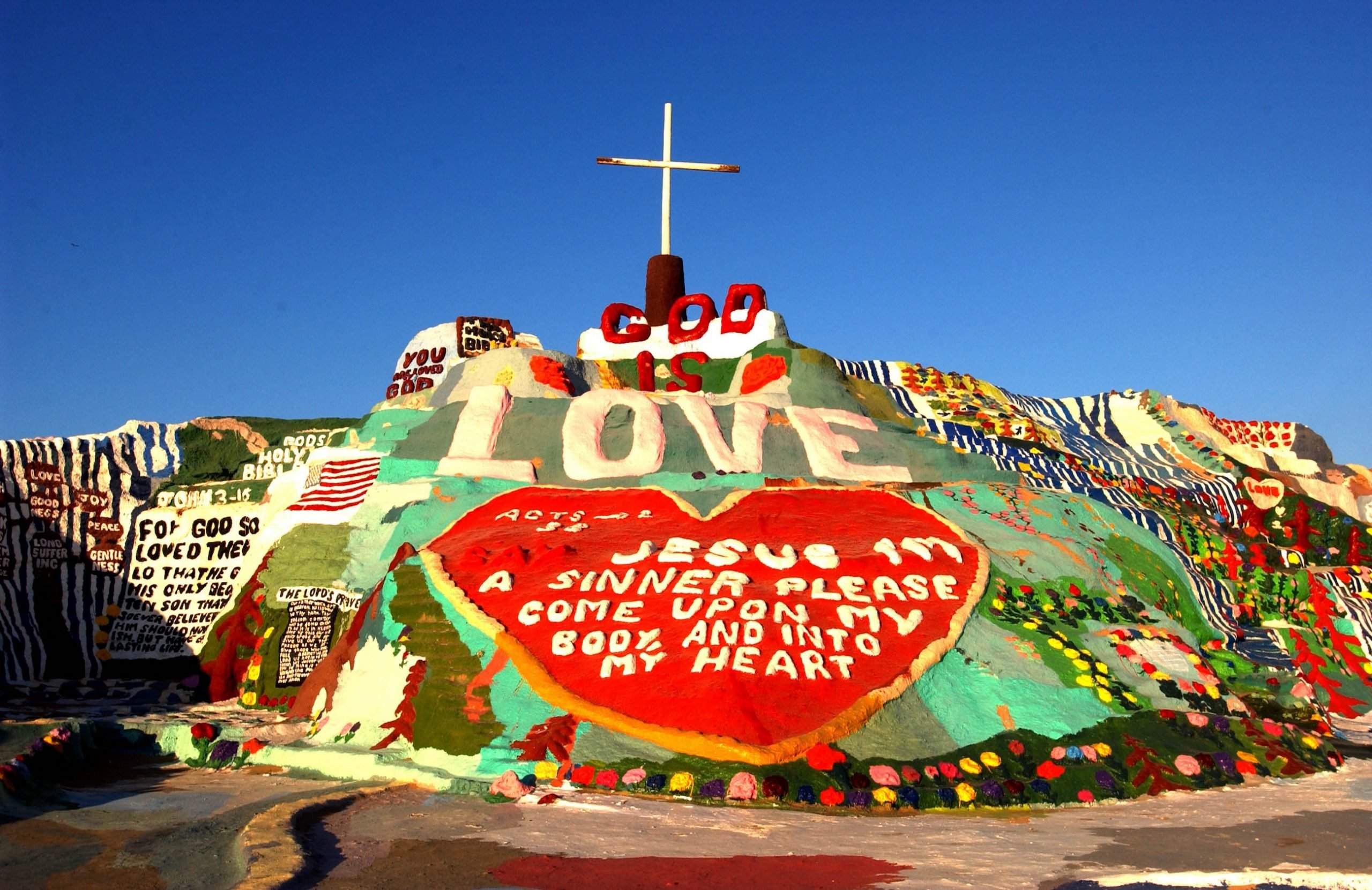 A giant outdoor artwork featuring a mountain of cement topped by a cross