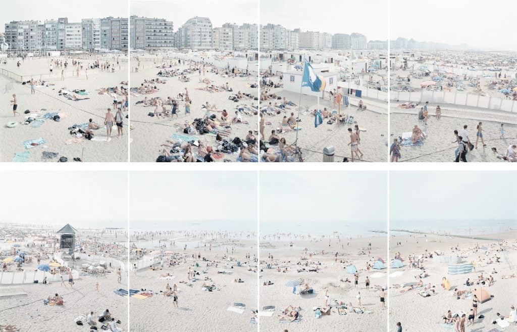 An 8 part photograph by Massimo Vitali showing a continuous panoramic view of a sandy beach with numerous beachgoers dotted along it.