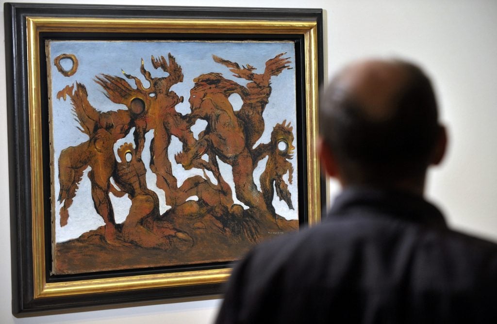 A man looking at Max Ernst's painting, La Horde, featuring various figures against a dusky sky