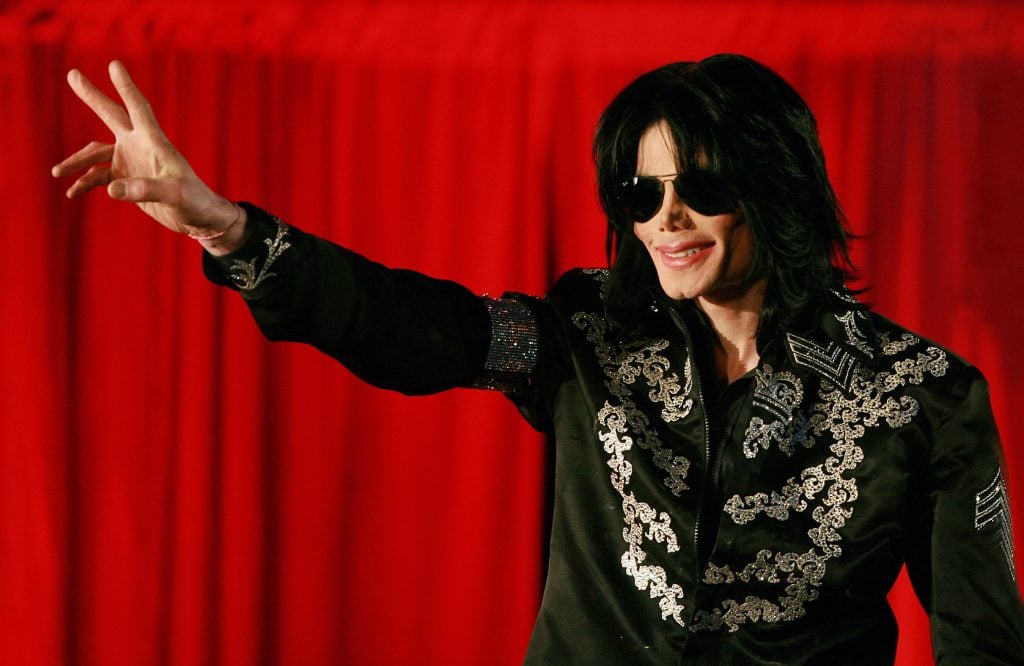 Pop star Michael Jackson in sunglasses and a black jacket throwing the peace sign