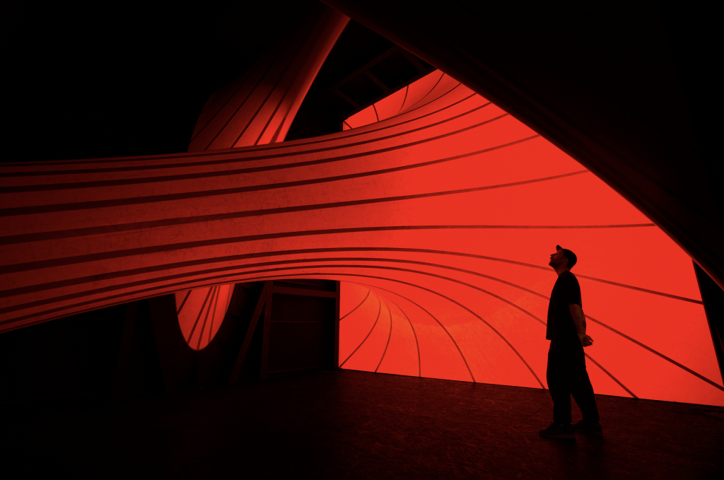 A photograph of the dark interior of a sculpture, with only a large glowing red tube and the silhouette of a viewer visible