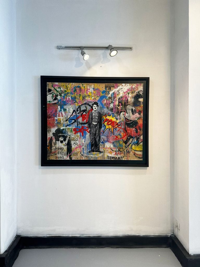 Mr. Brainwash artwork featuring a central figure of charlie chaplin surrounded by street art style collage and spray paint style additions.