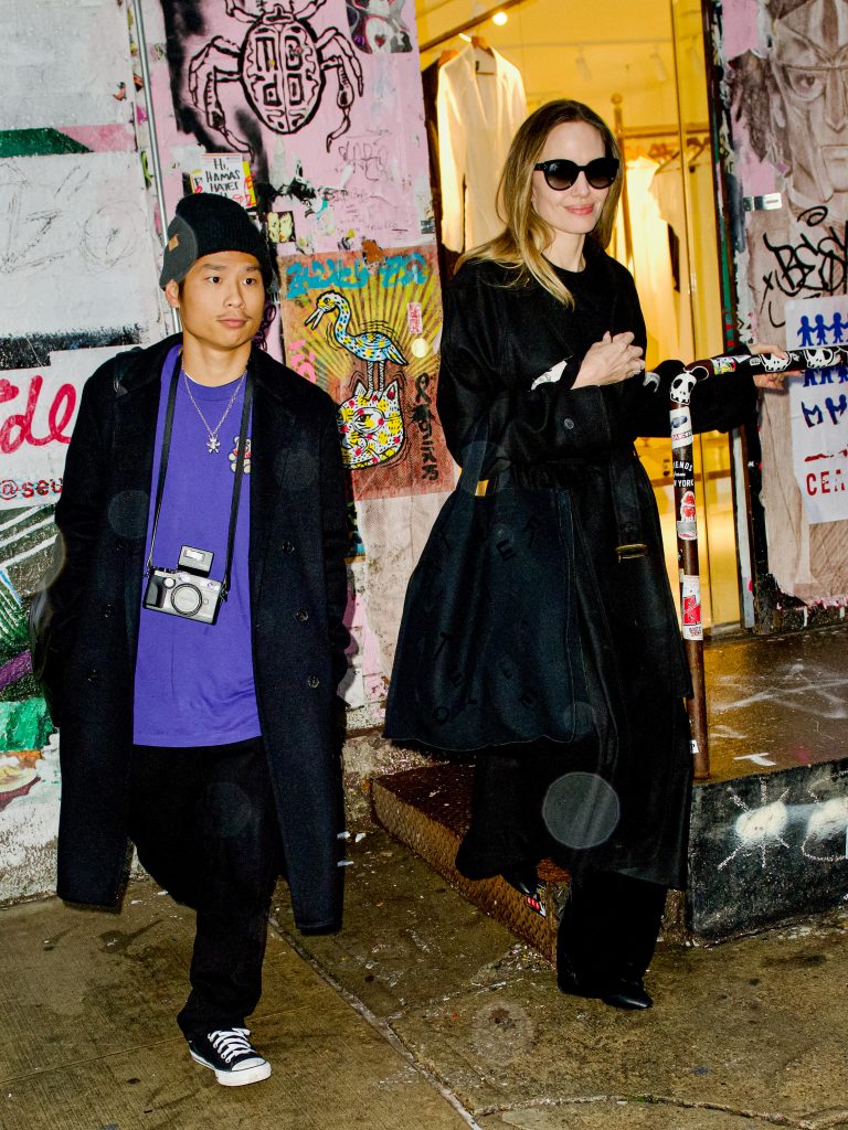 A woman in sunglasses, actor Angelina Jolie, emerging from a store front alongside a young boy, her son Pax Jolie-Pitt