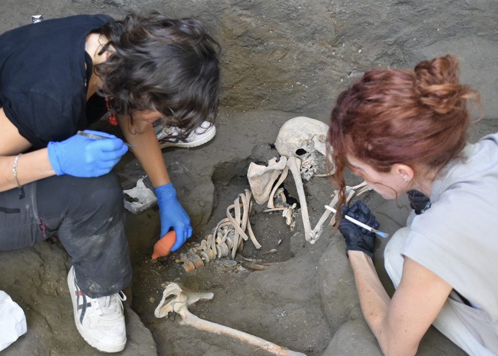 A photograph of two archaeologists unearthing a skeleton from the ground