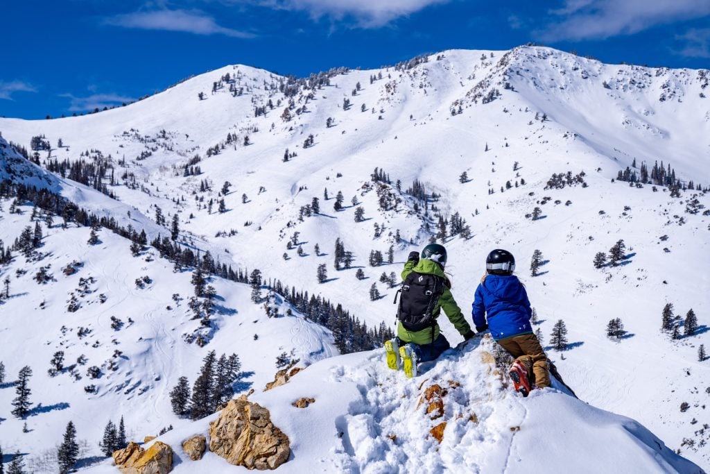 A photo of two skiers on a mountaintop, looking toward another in the distance