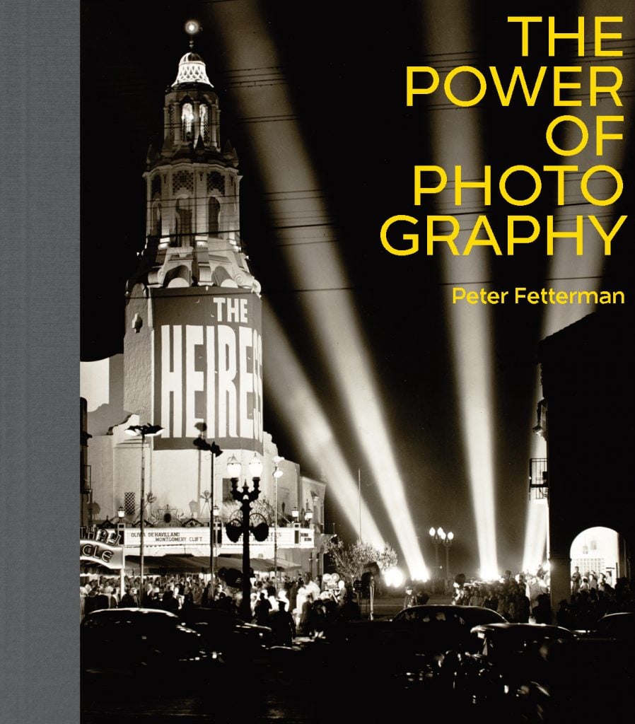 Book cover of Power of Photography by Peter Fetterman, published in 2022, with a gray fabric binding and a black and white photo of a vintage movie premier with four spotlights pointed up into a black sky, with the title of the book in yellow block letters at the top right.