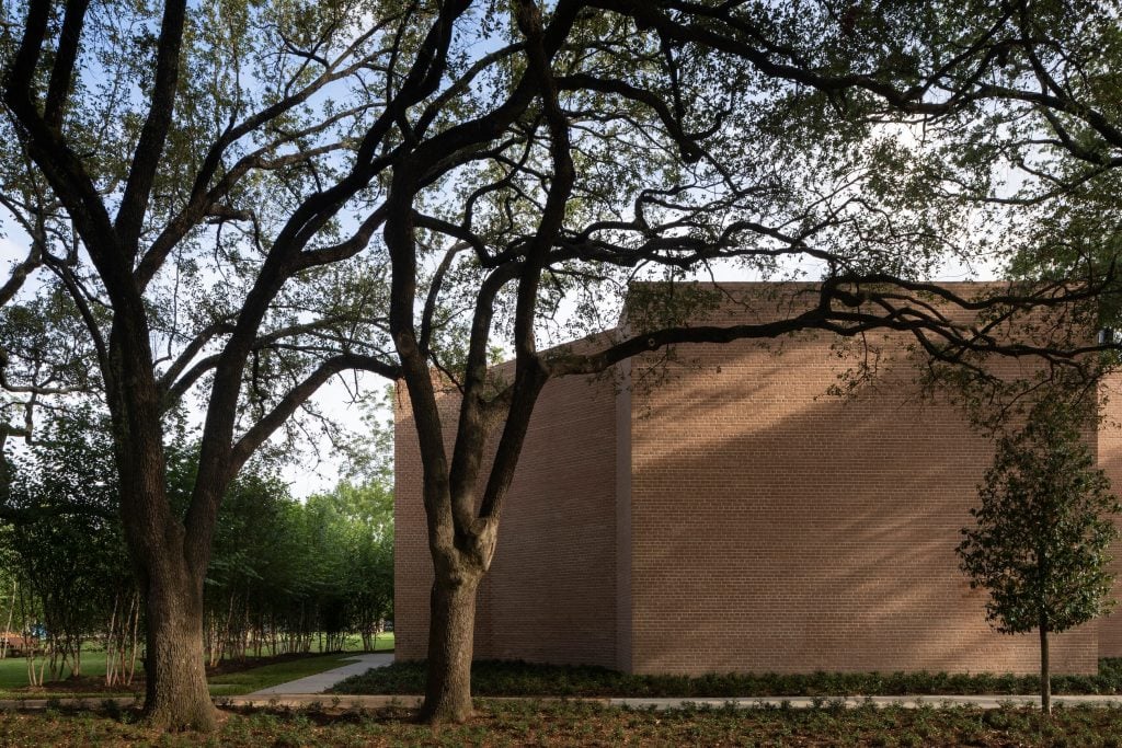 The brick exterior of a building, in a grassy setting with trees