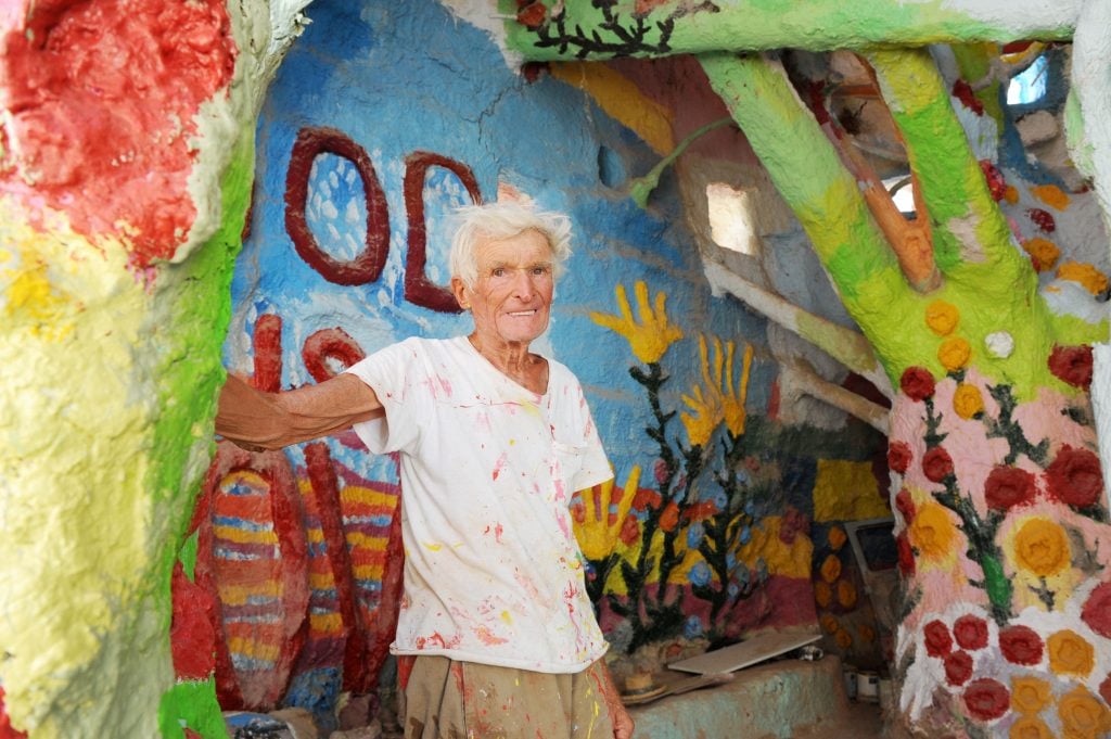 An elderly man stands inside a colorful art installation