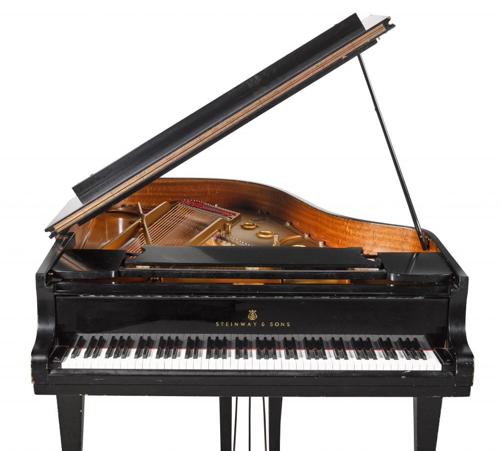 A photograph of a black grand piano with its top open, on a white background