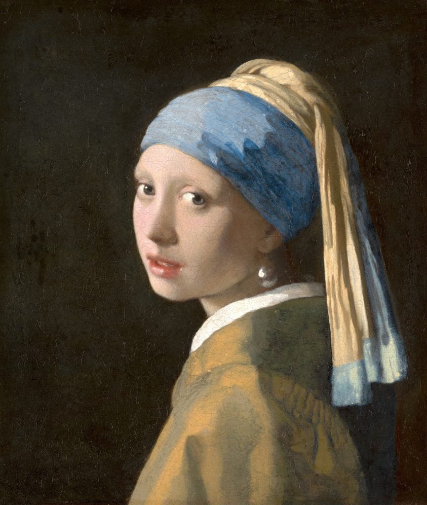 a painting of a woman in profile turning to look at us, she has her hair pulled back in a wrapped cloth that is blue and yellow and she is wearing a large pearl earring