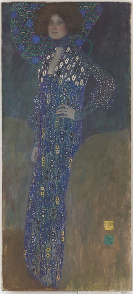 a painting of a woman in a blue gown with gold abstract shapes. the woman has black voluminous hair.