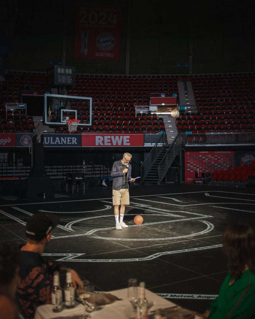 Michael Buhr speaks at the opening of the Various others art event, at the dinner on a basketball court