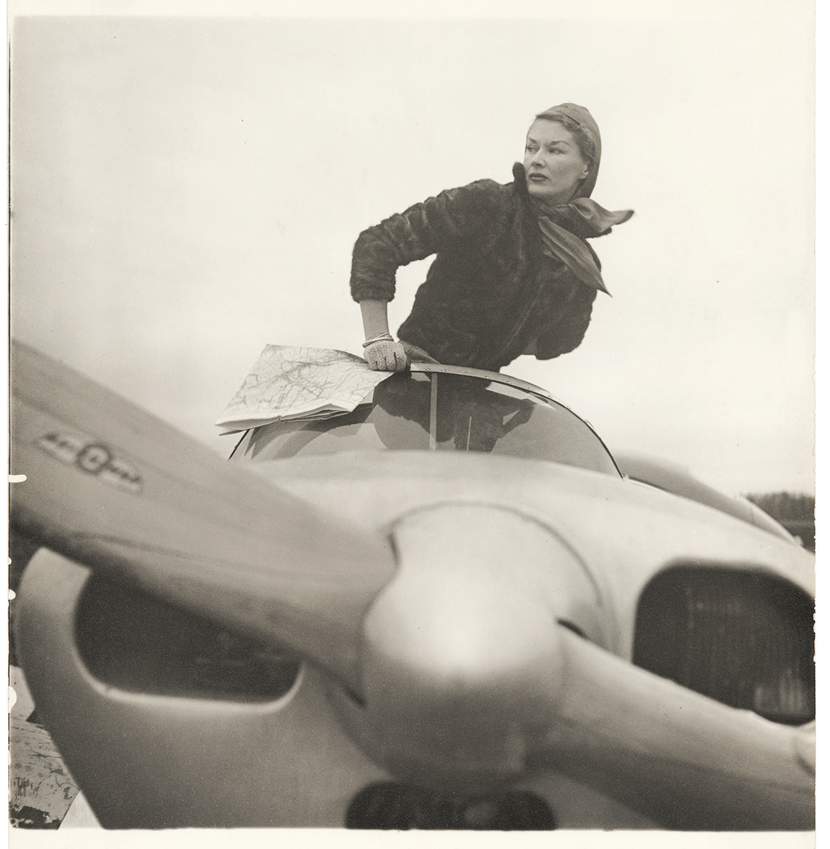 a black and white photo of supermodel Lisa dressed as Amelia Earhart, posing in an airplane