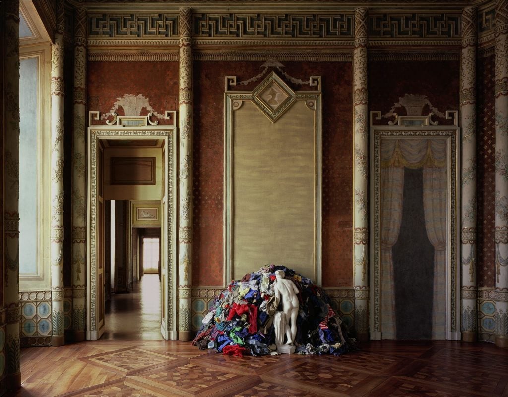 royal looking interior space with a work by michelangelo pistoletto showing a marble statue facing a pile of clothes