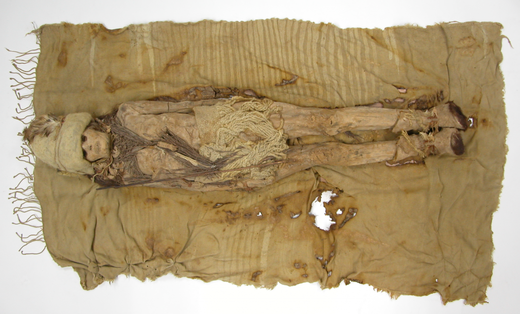 Ancient mummy wrapped in cloth, laid out on a weathered blanket.