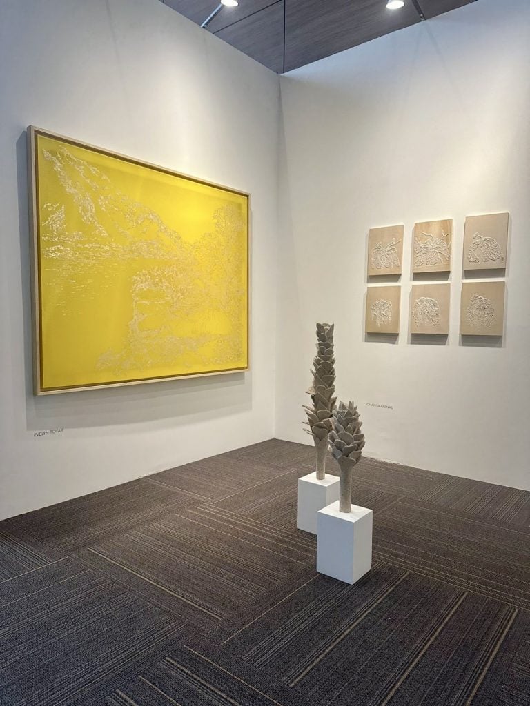 a yellow painting is next to gray sculptures in a gallery 