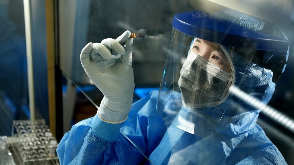 Scientist in protective gear analyzing a small sample in a laboratory.