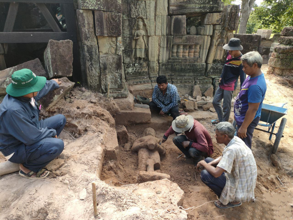 a group of men are gathered around a statue with the temple wall to the back