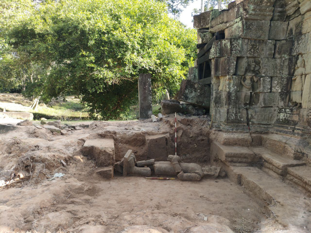 a statue in the ground with a temple to the right hand side and trees to the back