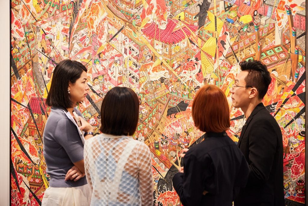 An intricate painting hangs in a booth. People stand near it.