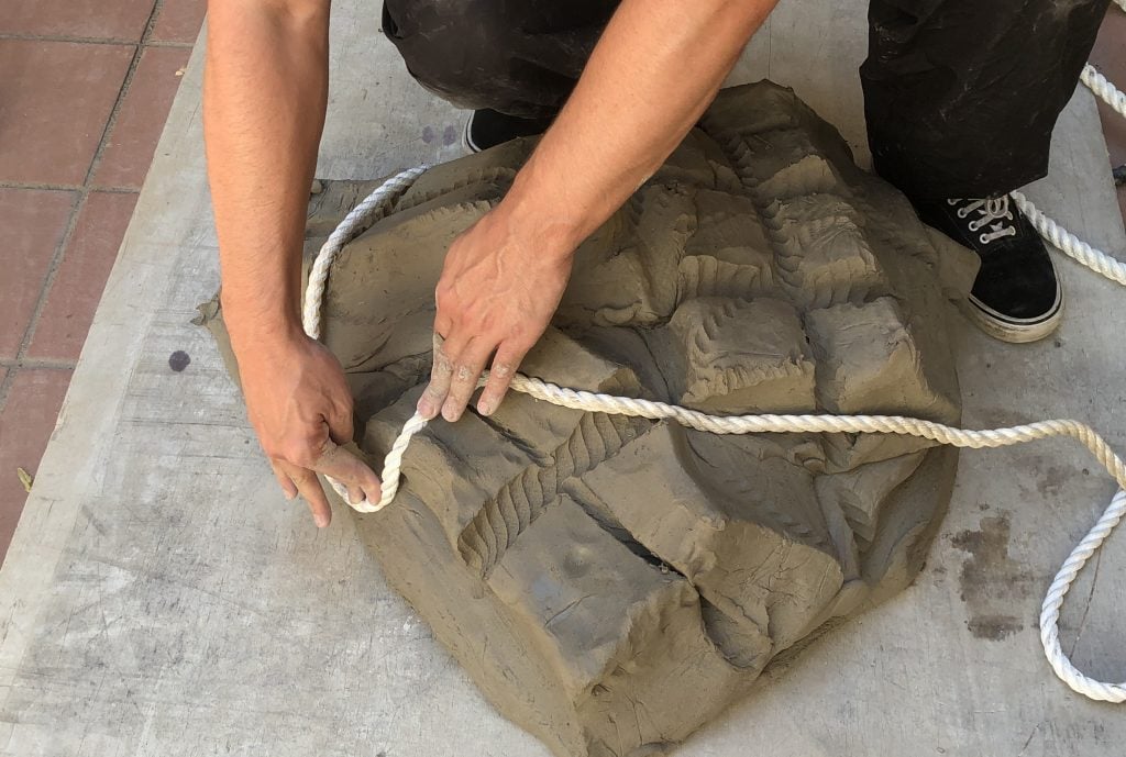 a man's hands are seen working and moulding a large lump of clay that has patterns in its surface created using a length of rope