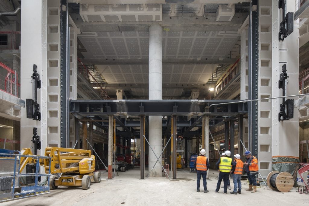 three men in hi-viz vests and hard hats stand outside of a building under construction