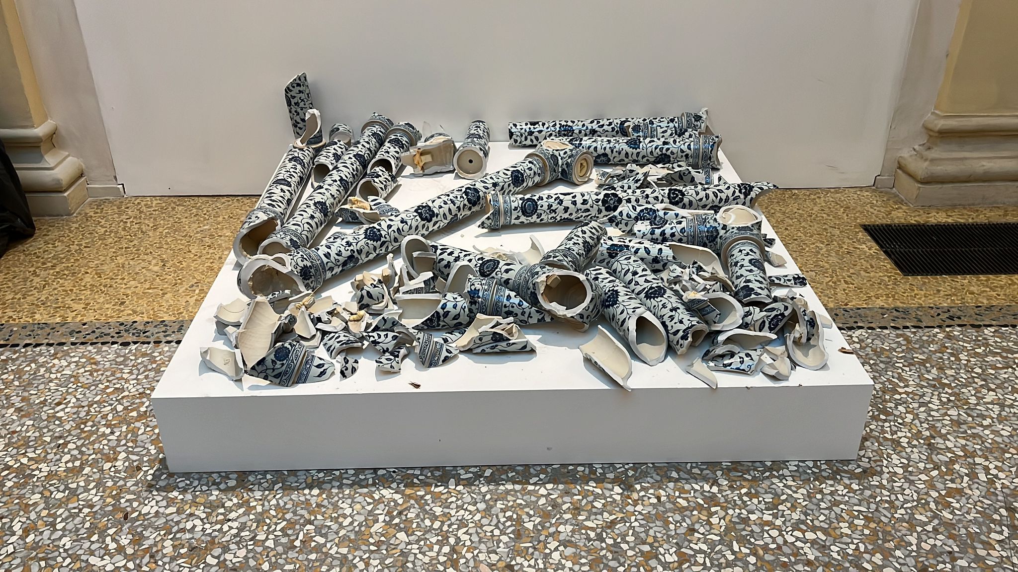 fragments of blue and white ceramics, of which large pieces have a long, hollow tube-like shape, can be seen gathered together on a raised white podium