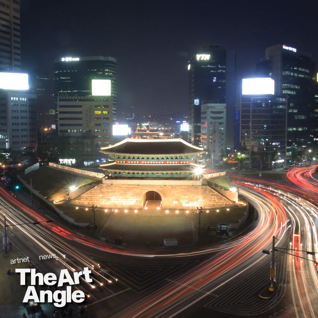 a timelapse view of one of the iconic gates in the center of Seoul is lit up against a backdrop of modern skyscrapers