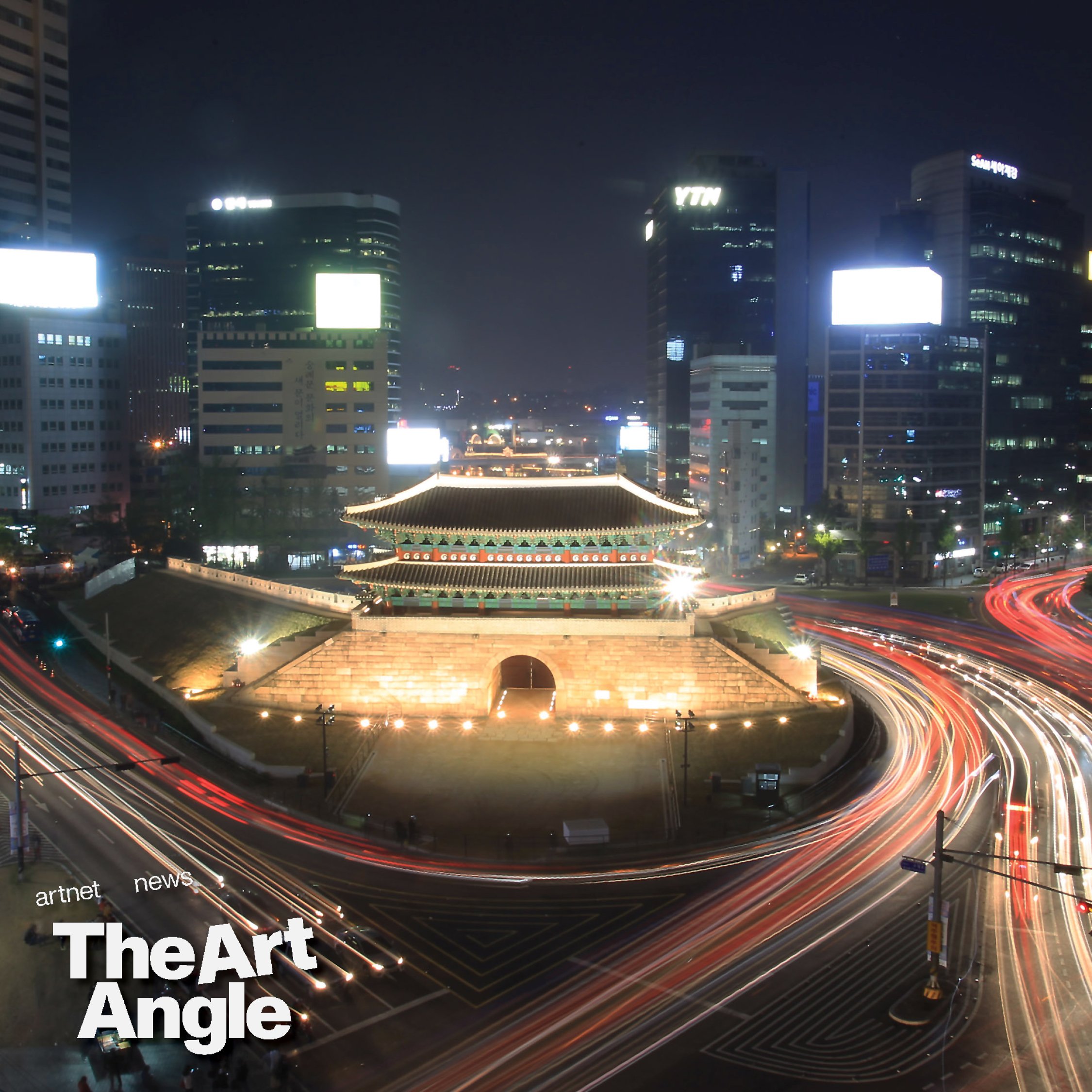 a timelapse view of one of the iconic gates in the center of Seoul is lit up against a backdrop of modern skyscrapers