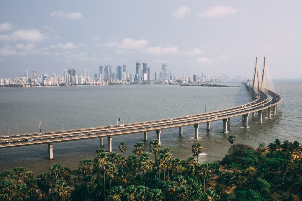 This image depicts a city's coast line, connected to a piece of land full of trees with a very long bridge.